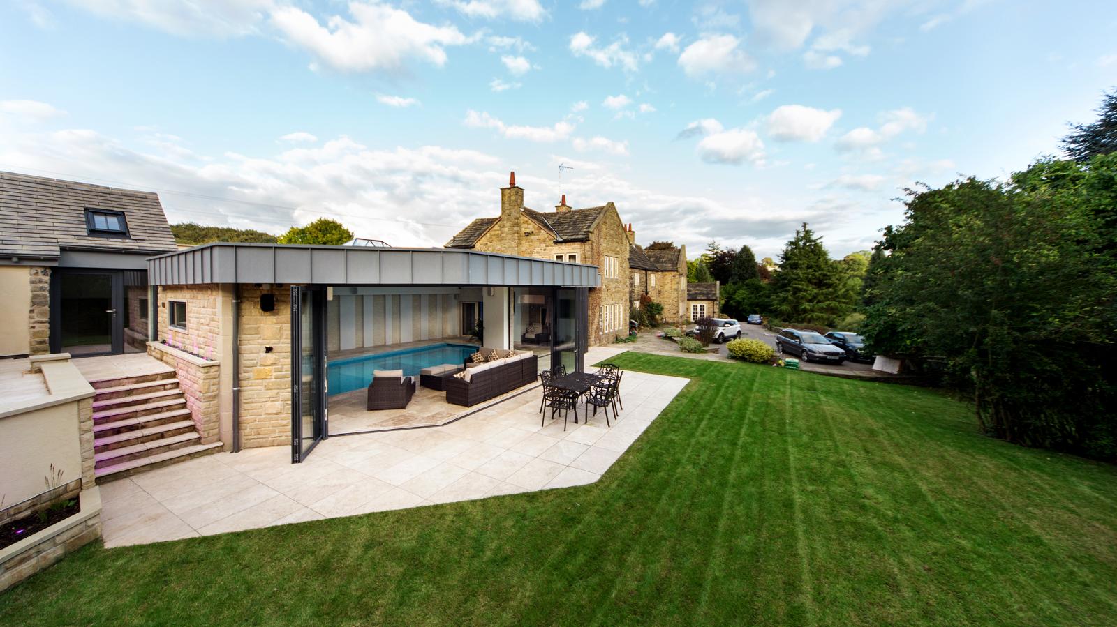 Completed single-storey rear extension in natural stone with a zinc-effect flat roof and bi-fold doors onto a garden