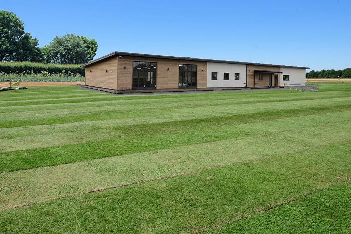 Completed single-storey new build house with timber cladding and full-height glazing set in open Lincolnshire countryside
